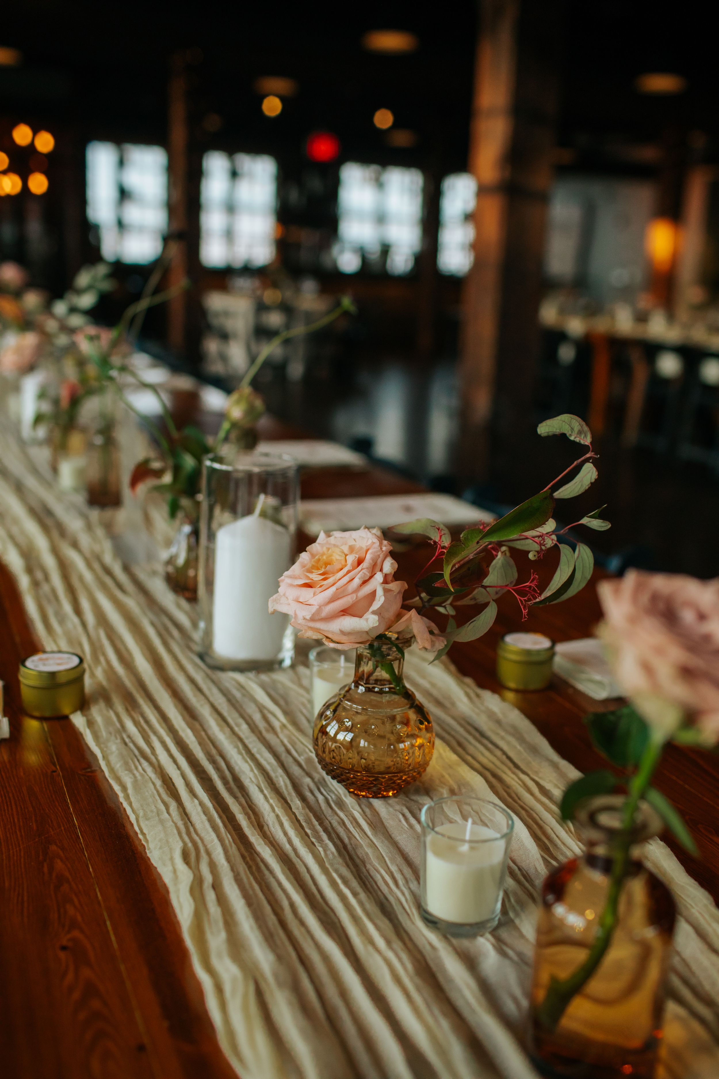 Elegant table decor with pink roses and white candles arranged on a rustic wooden surface with draped fabric.
