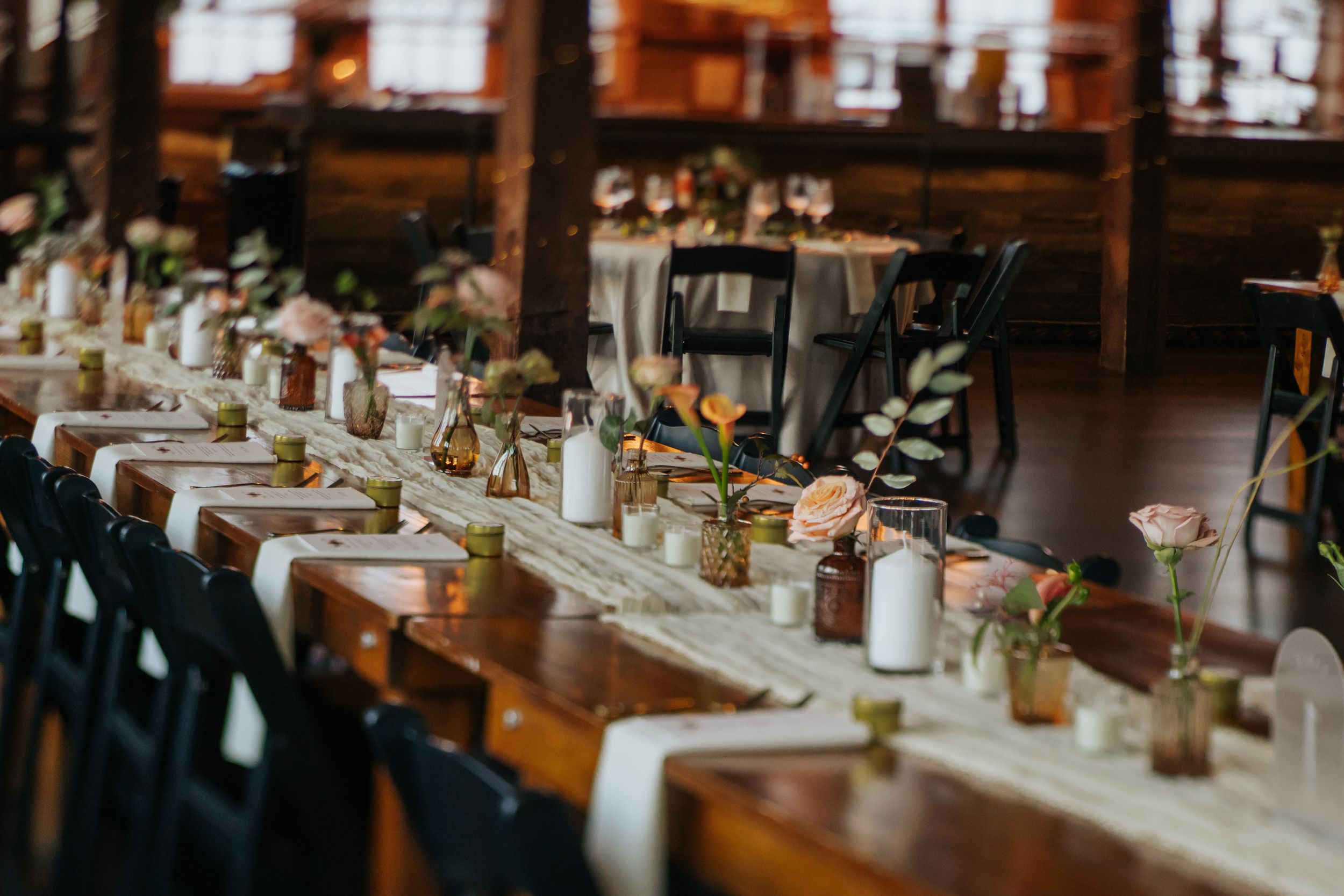 Elegant rustic restaurant interior with wooden tables set for dinner service featuring white tablecloths and floral centerpieces.