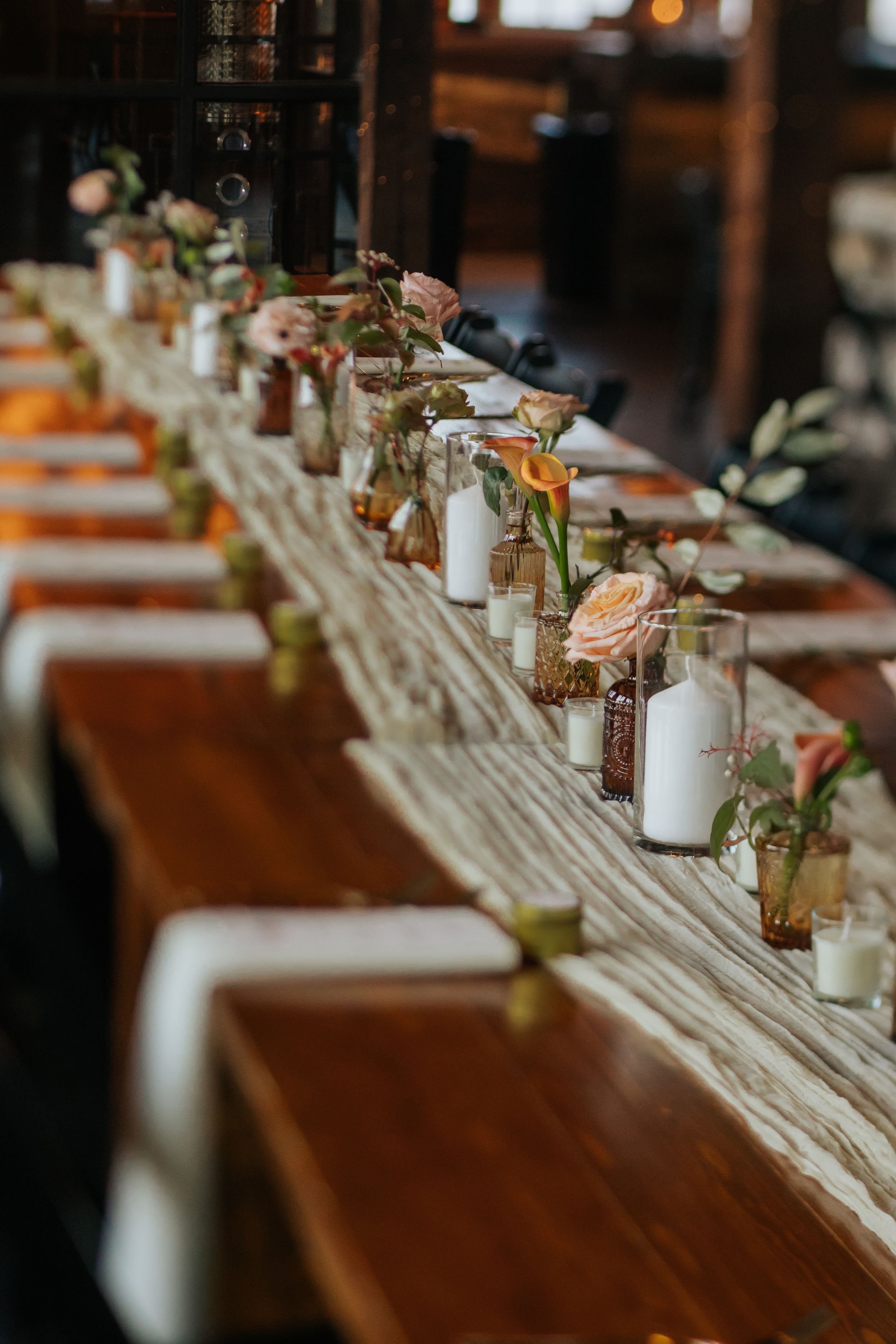 Long rustic wooden table decorated with elegant candles and floral centerpieces for a wedding reception.