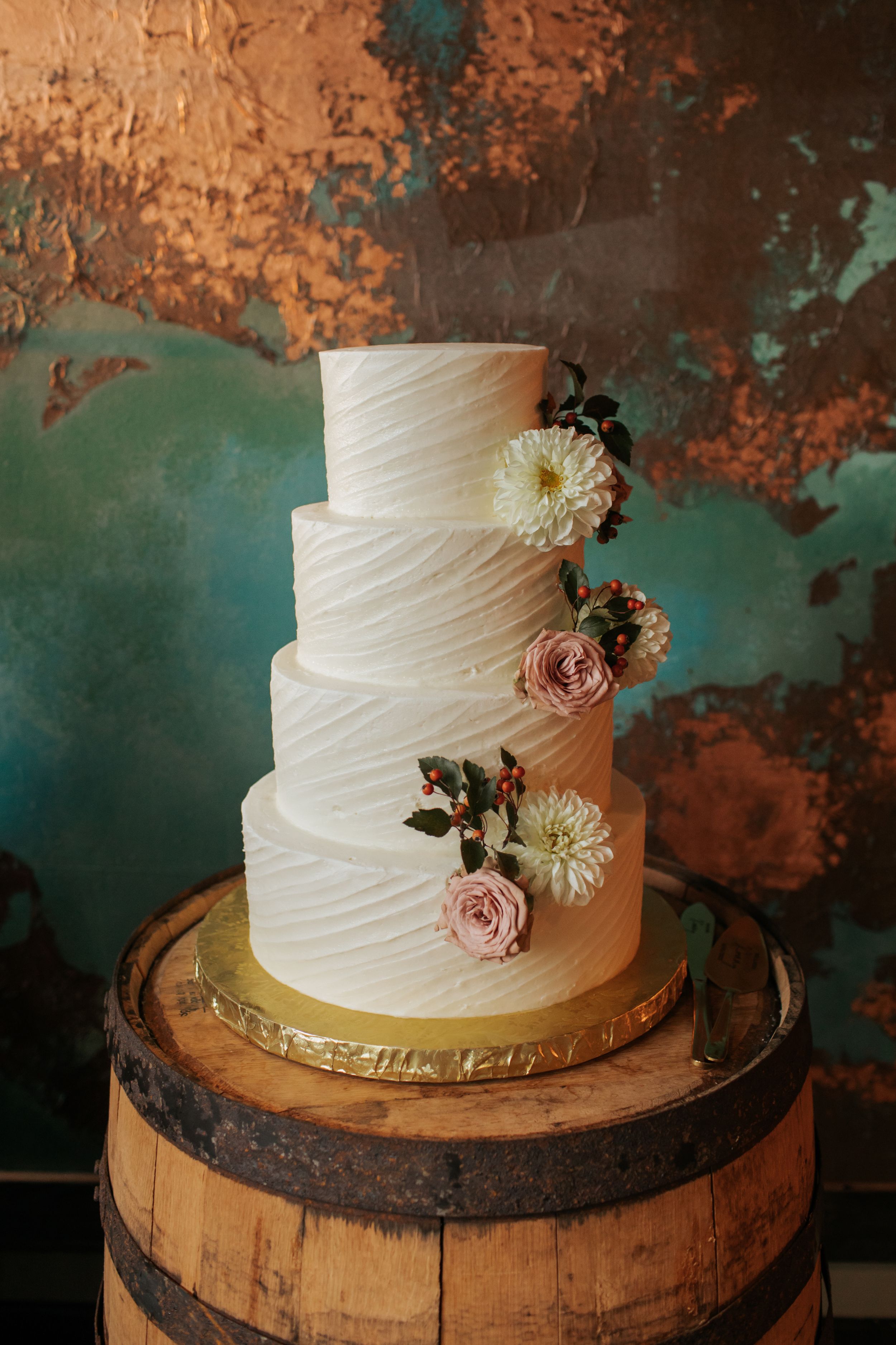 White wedding cake with textured frosting and pink floral accents displayed on a rustic wooden barrel.