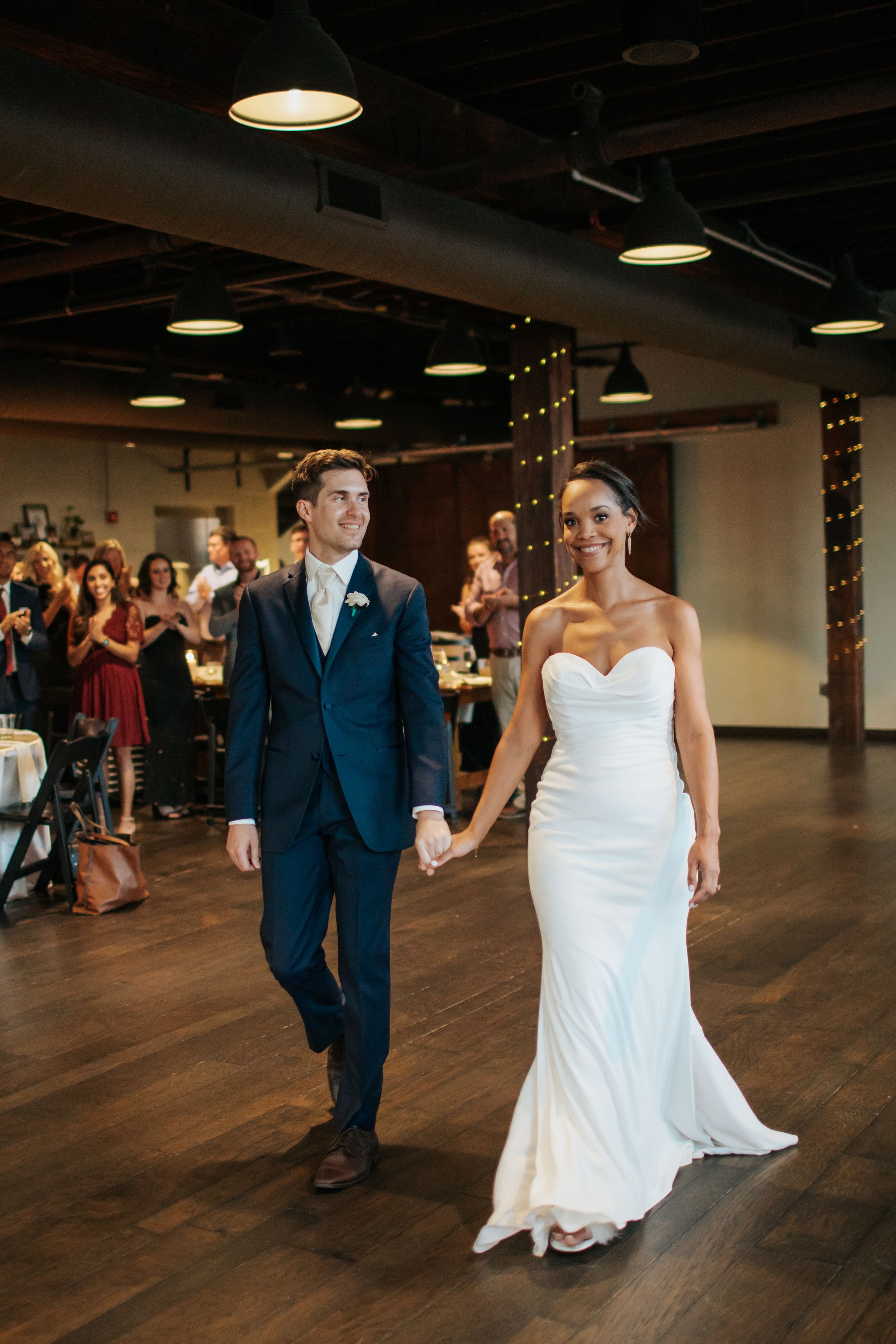 A couple dancing together at their wedding reception in a rustic venue with wooden floors and industrial lighting.