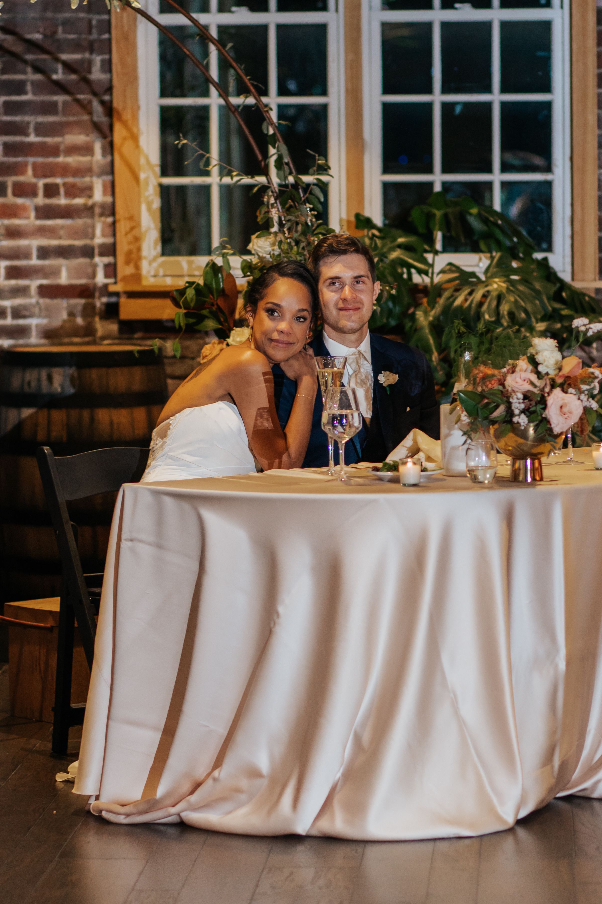 Wedding reception table setup with white linens in an industrial-style venue with exposed brick walls.