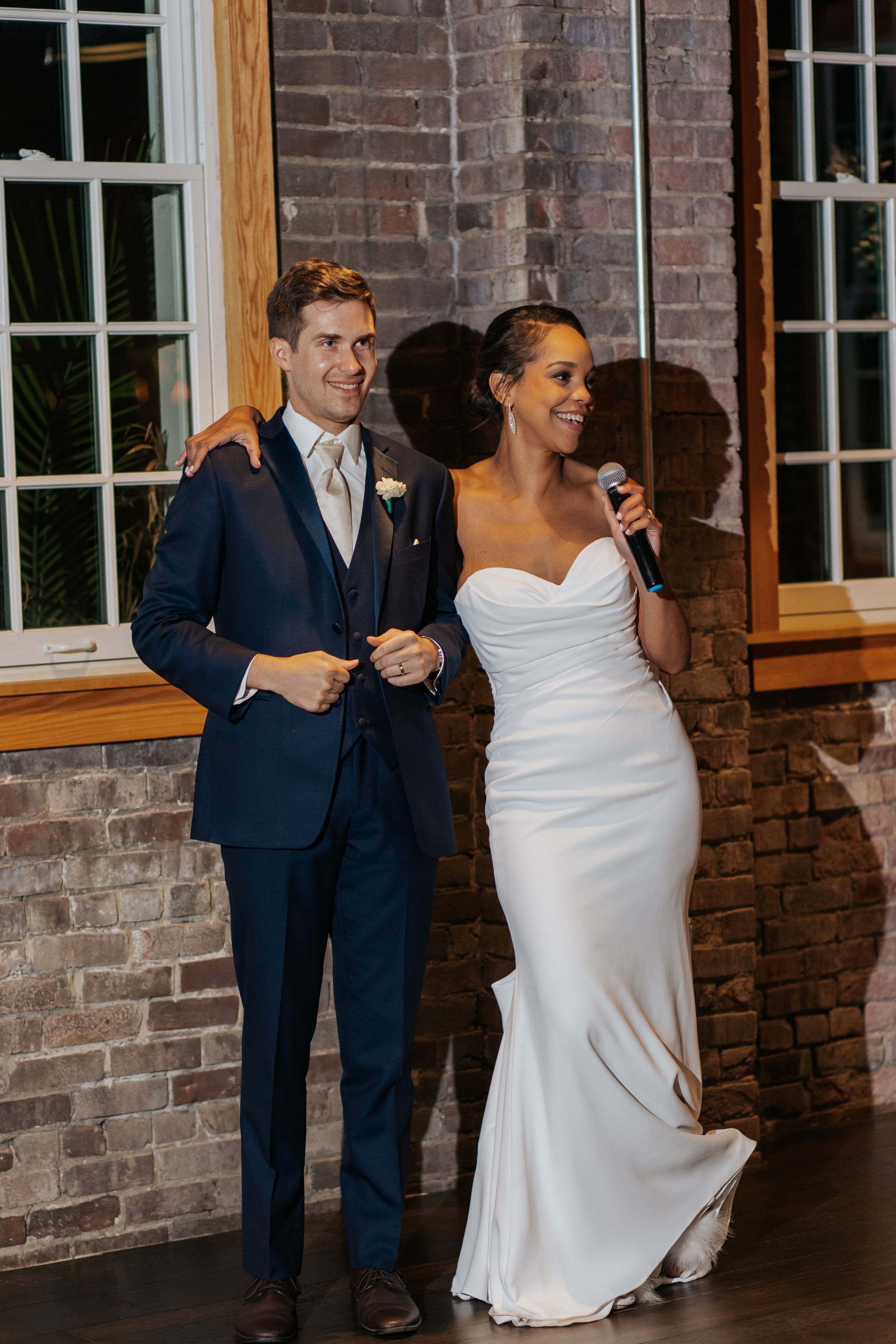 Wedding couple dances together in an elegant indoor venue with exposed brick walls and windows.