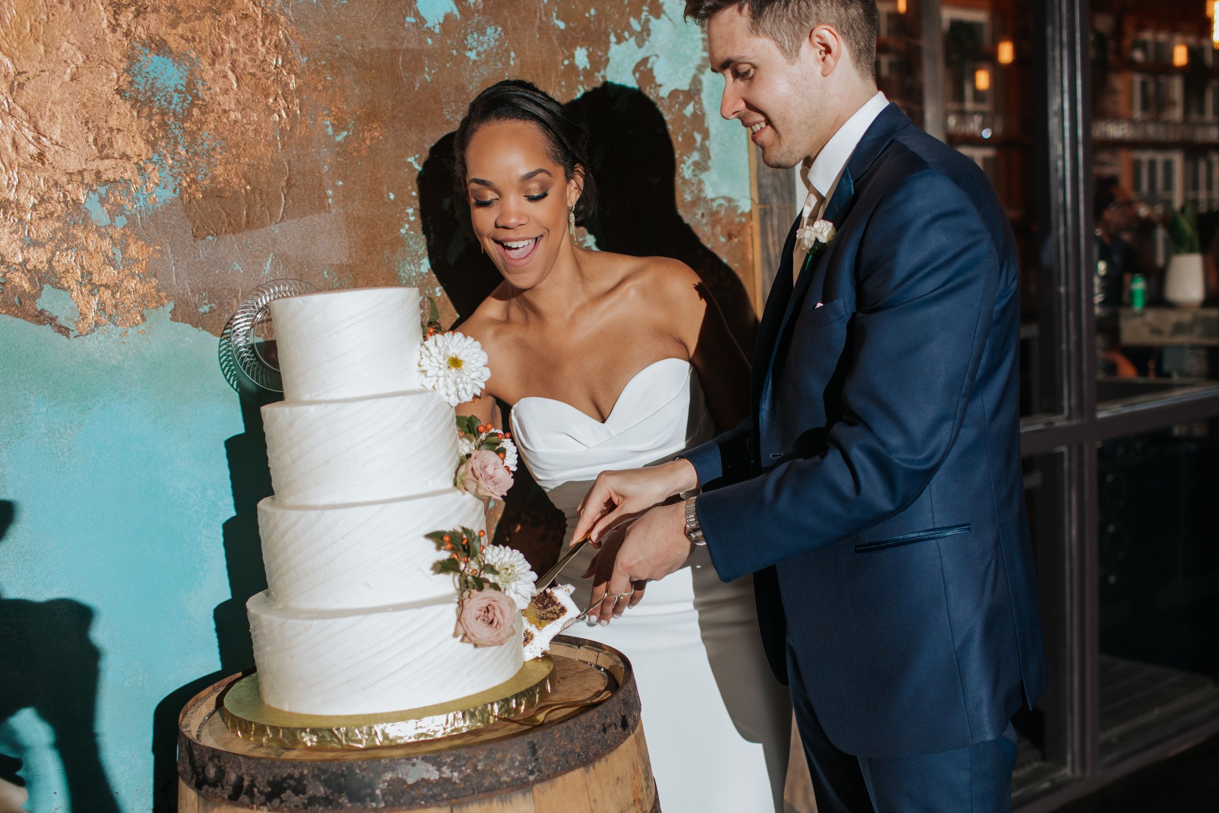 Wedding cake cutting moment in front of a distressed turquoise wall with vintage character.
