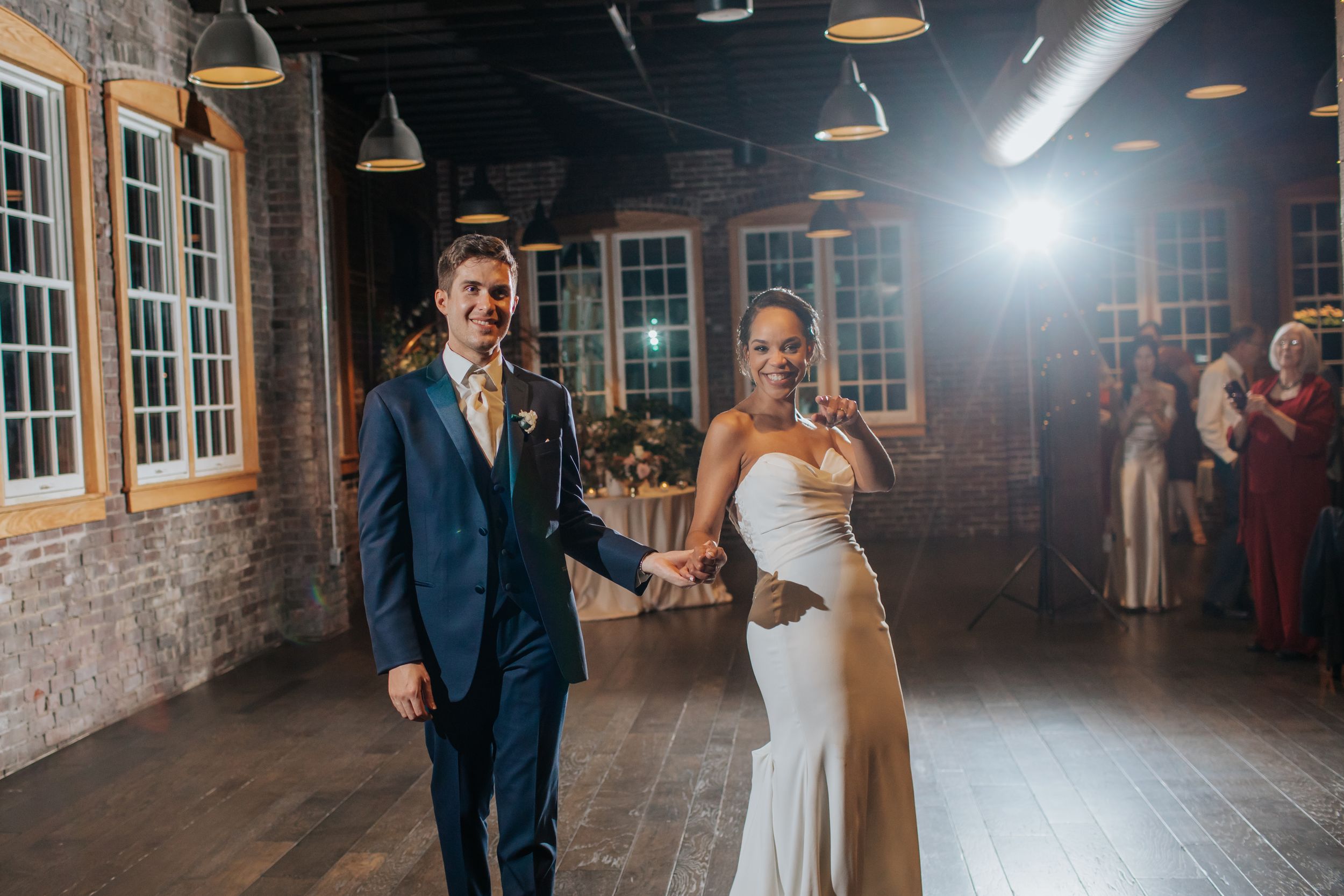 Couple dancing together in a dimly lit industrial-style venue with exposed brick walls and pendant lighting.