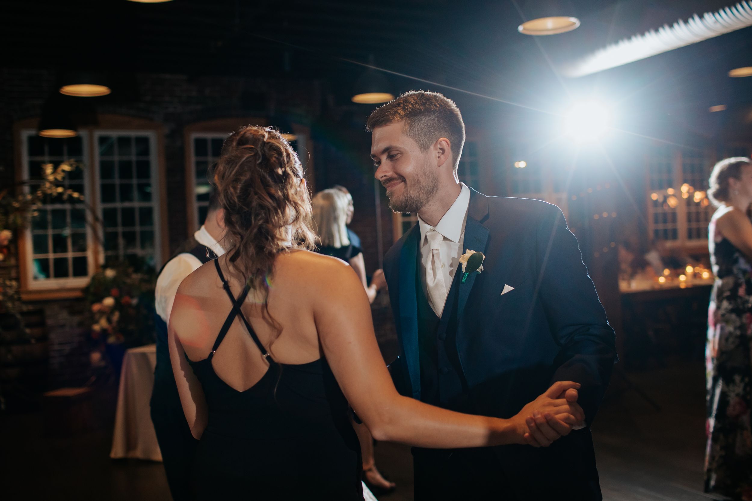 A couple shares an intimate dance moment in a dimly lit reception venue with romantic lighting.