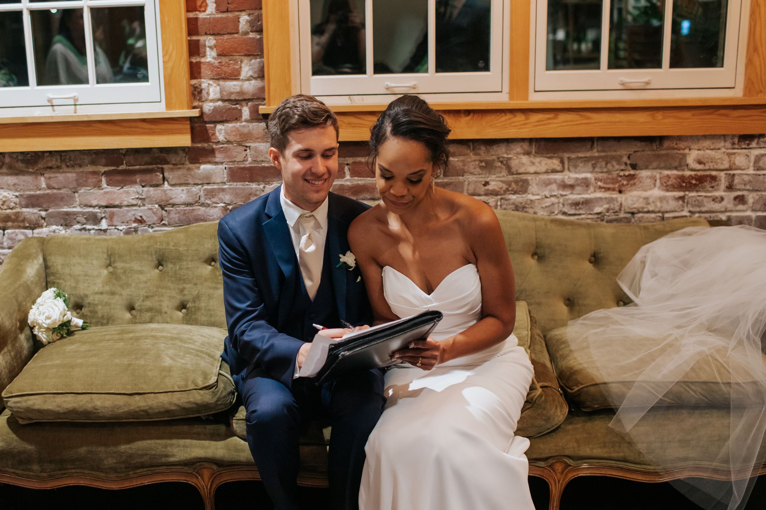 A couple sits together on a vintage green couch sharing a quiet moment at their wedding.