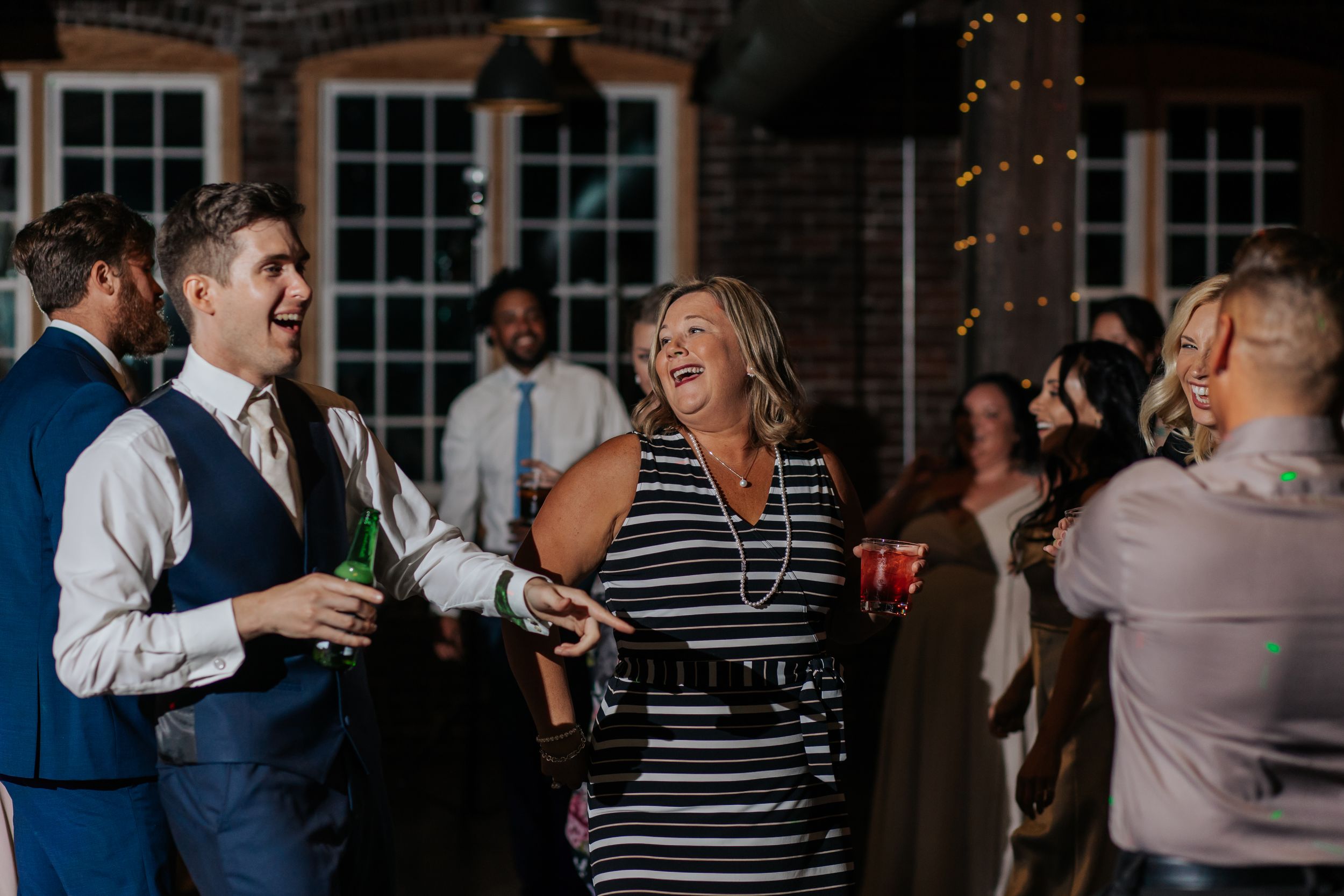 Wedding guests mingling and dancing during evening reception with string lights overhead.