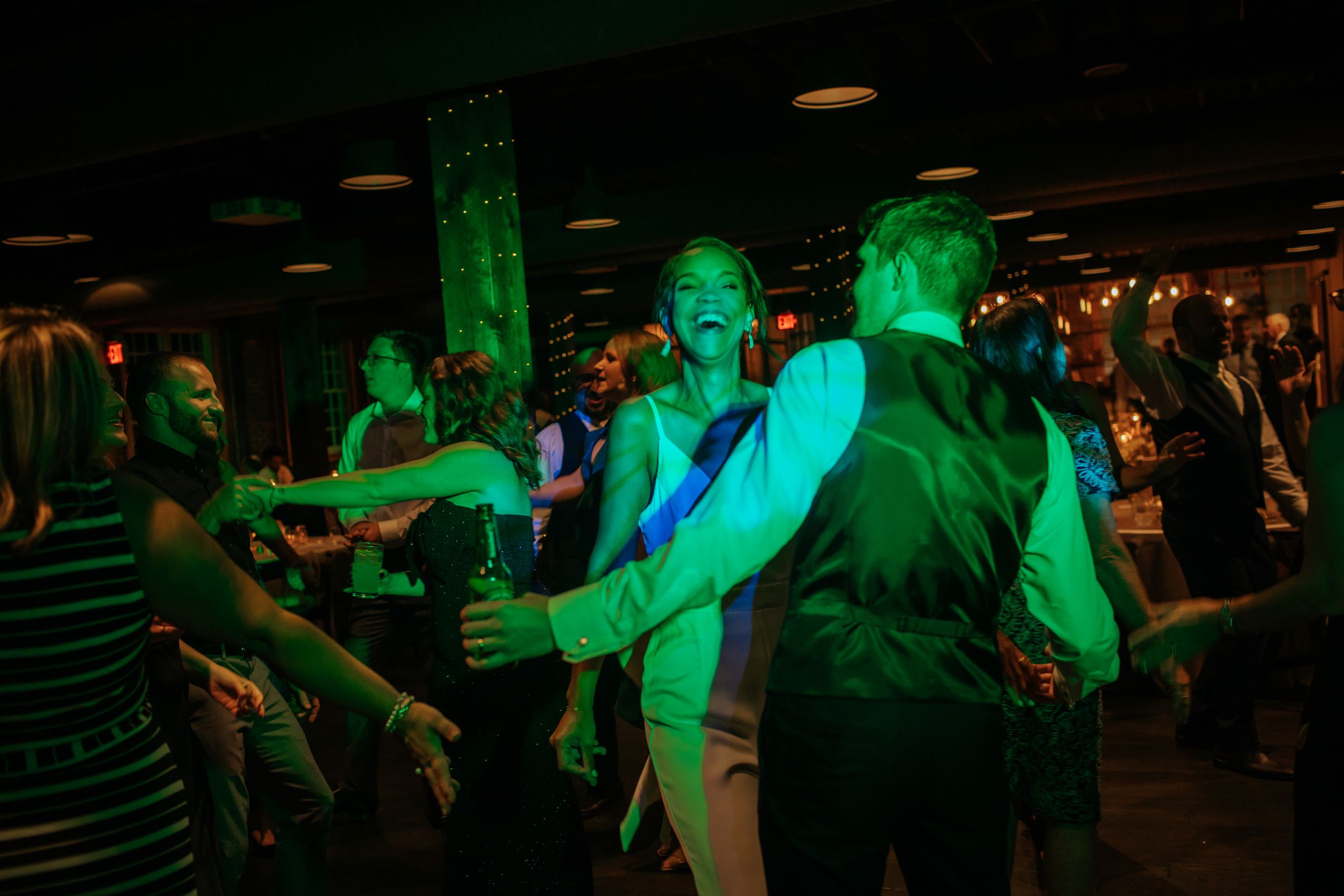 Wedding reception dance floor illuminated with green lighting as guests celebrate and dance together.