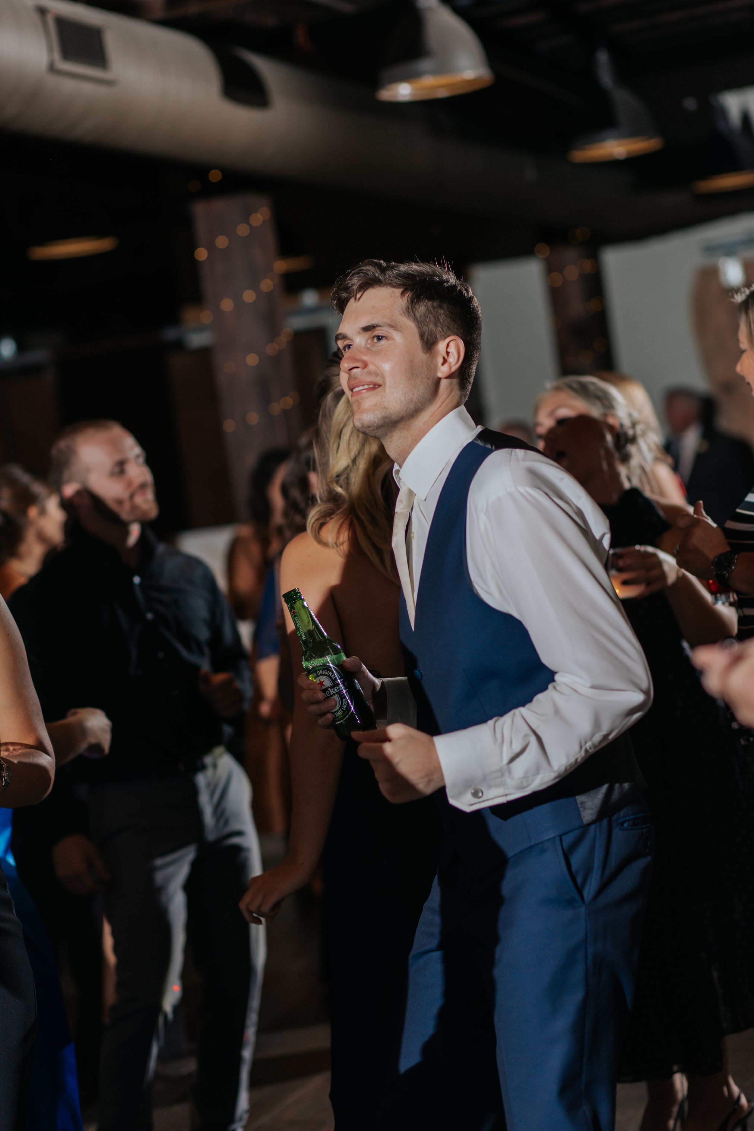 Wedding reception guests dancing and celebrating in a dark venue with ambient lighting.