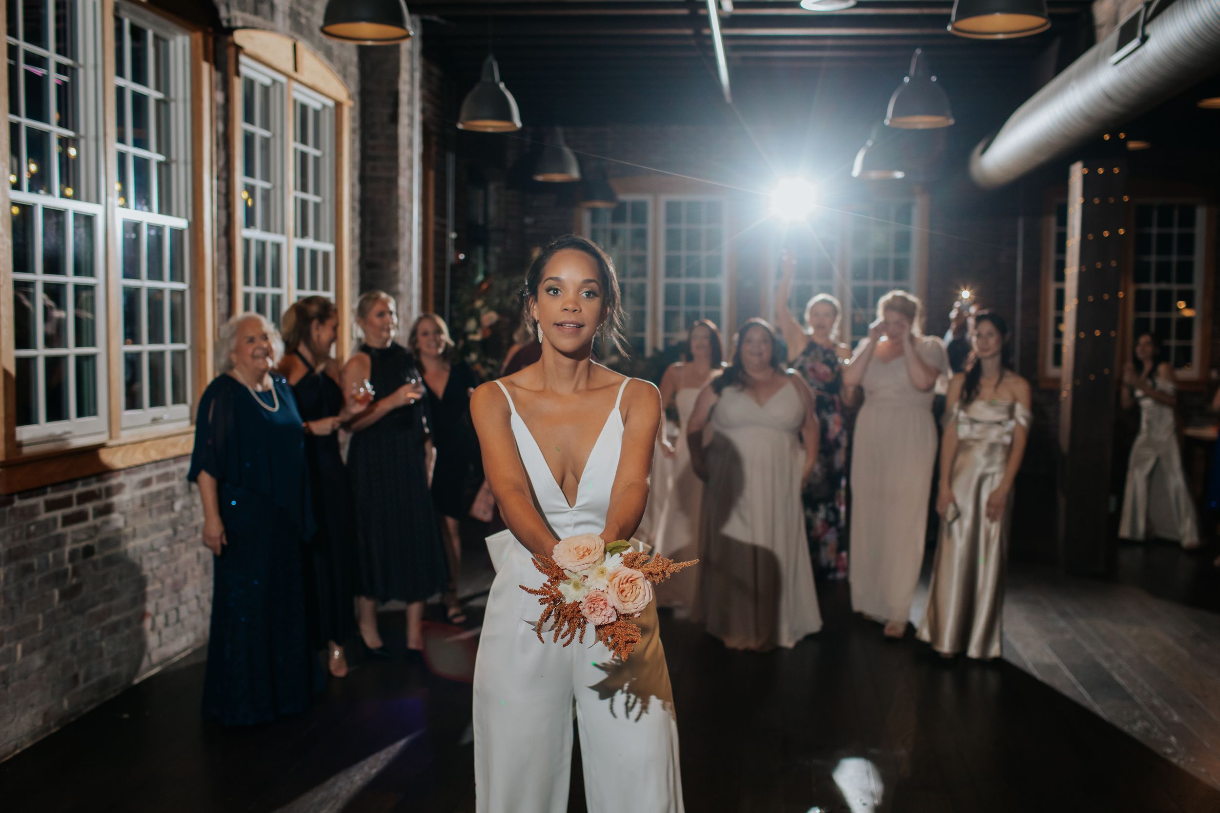 Wedding guests dance and celebrate on a dimly lit industrial-style dance floor with exposed brick walls and hanging lights.