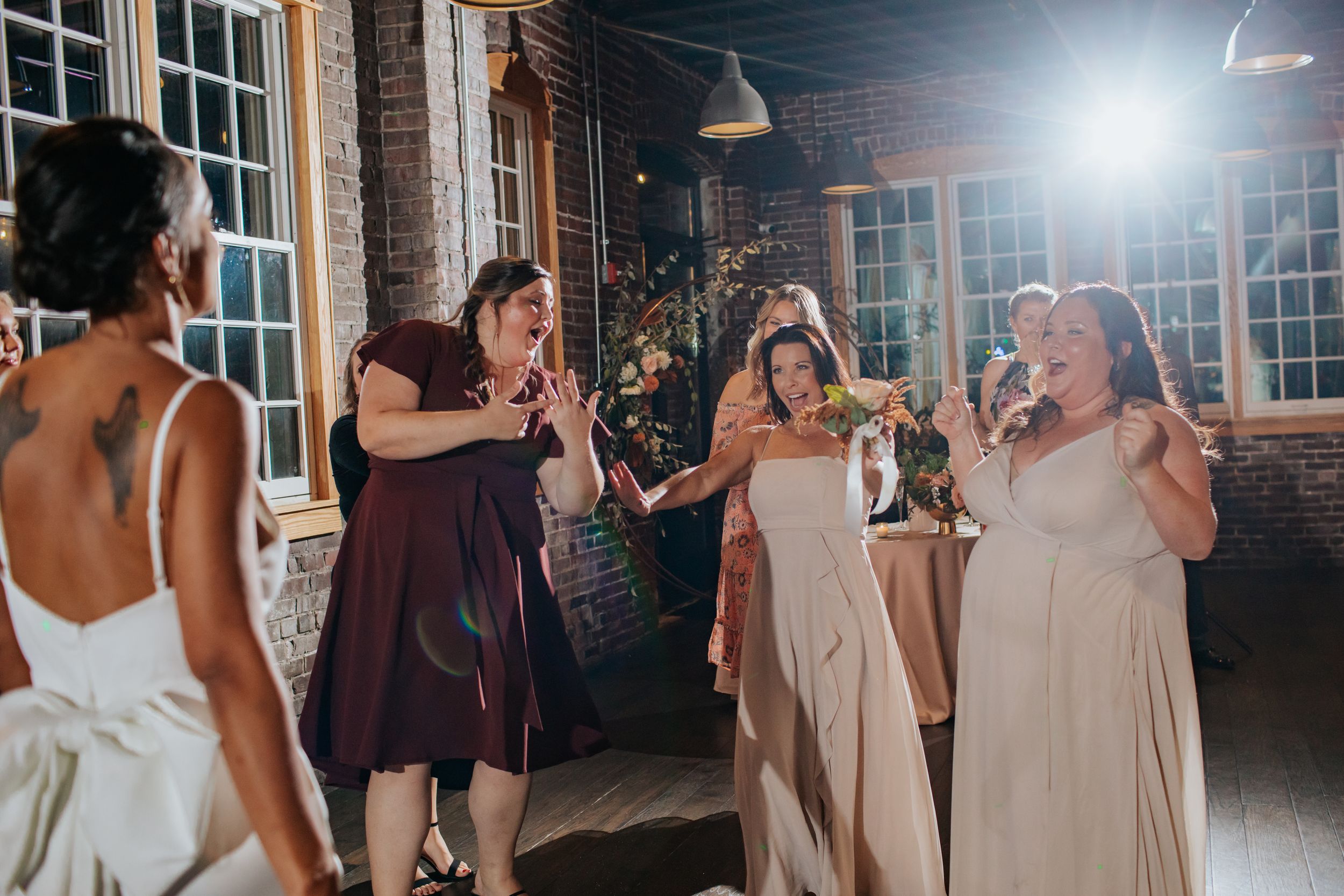 Wedding party celebrating on a dance floor in an elegant venue with large windows.