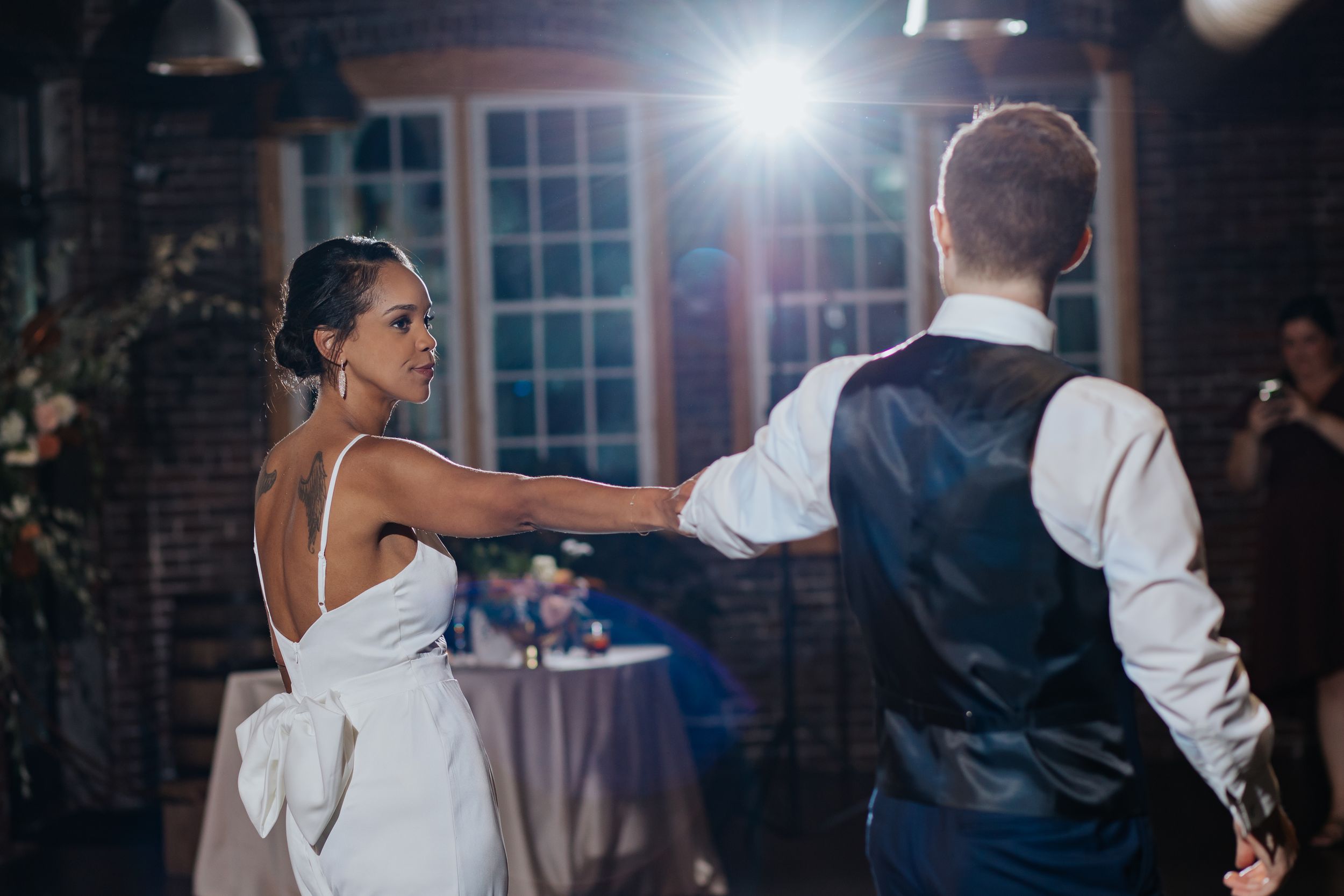 Wedding celebration with dancers silhouetted against bright lights in an industrial brick venue.