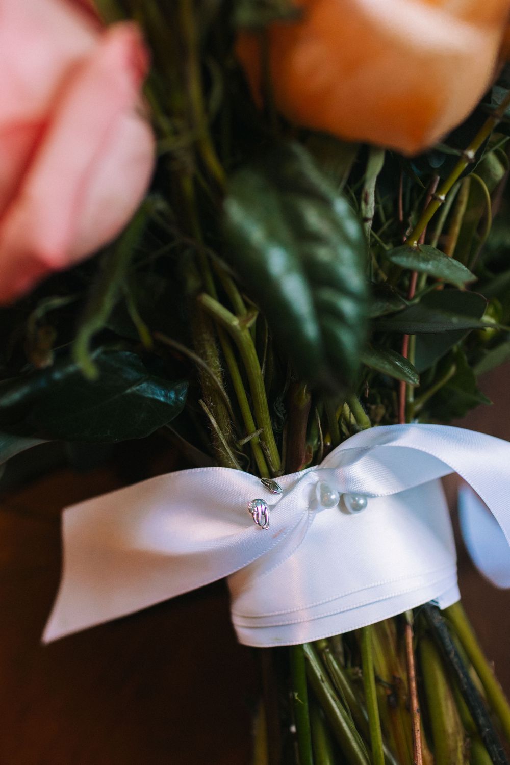 White satin ribbon being tied around a bundle of fresh green herbs or stems in a decorative arrangement.