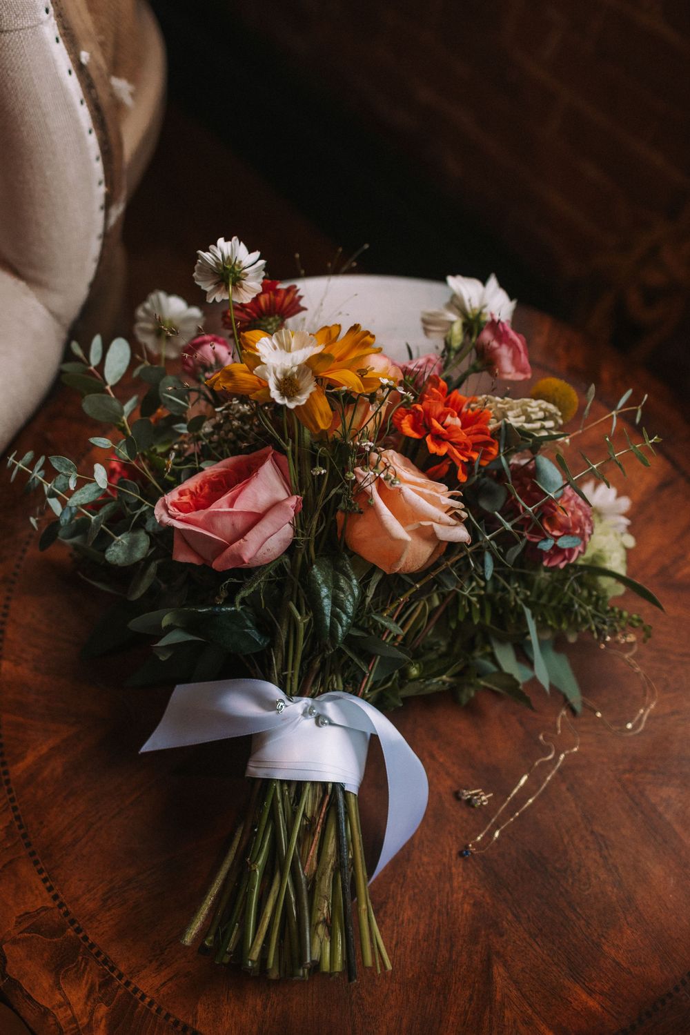 Progression of floral bouquet assembly showing colorful roses and wildflowers tied with white ribbon on dark wooden surface.
