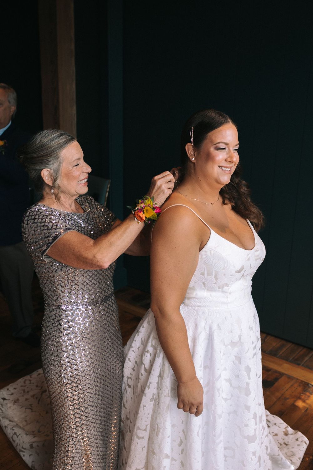 Two people share a joyful moment while getting ready, with one wearing a white dress and the other in a sparkly outfit.