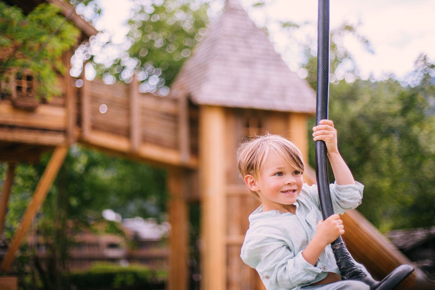 A young child smiles while playing on playground equipment at a wooden treehouse.