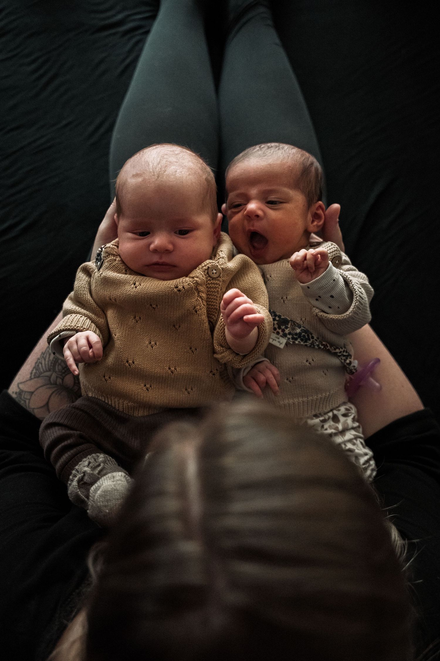 Four sequential photos show two sleeping newborn twins wearing matching brown outfits against a dark background.