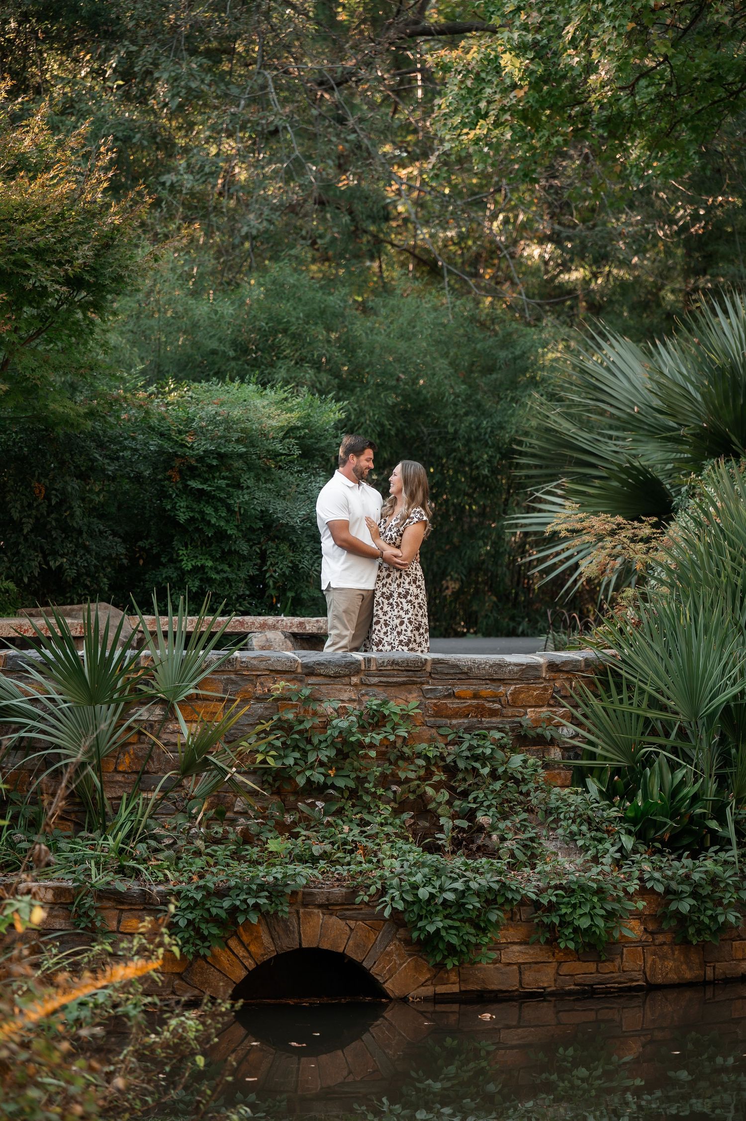 Couple sharing an intimate moment on a stone bridge over a garden pond.