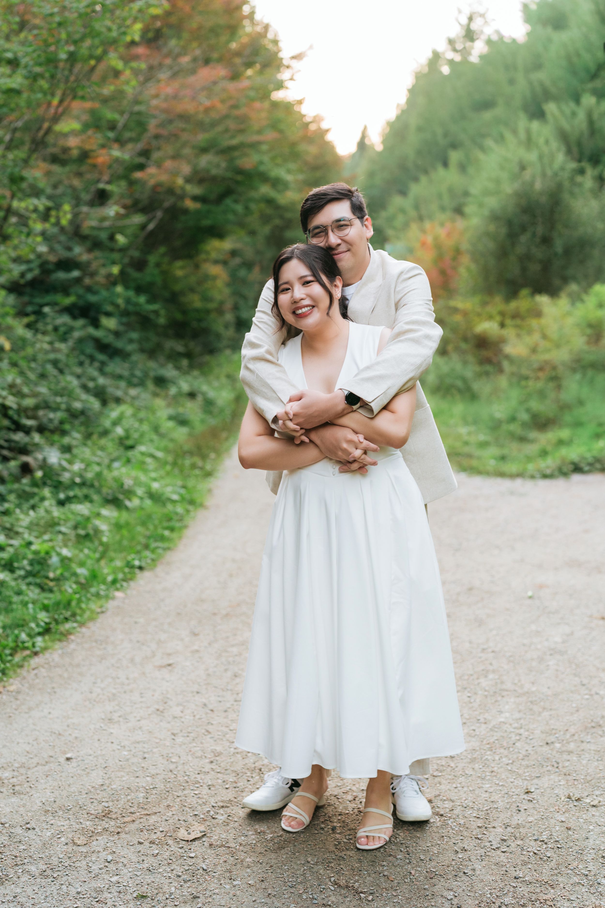 A couple shares a romantic embrace on a dirt path surrounded by autumn foliage and greenery.