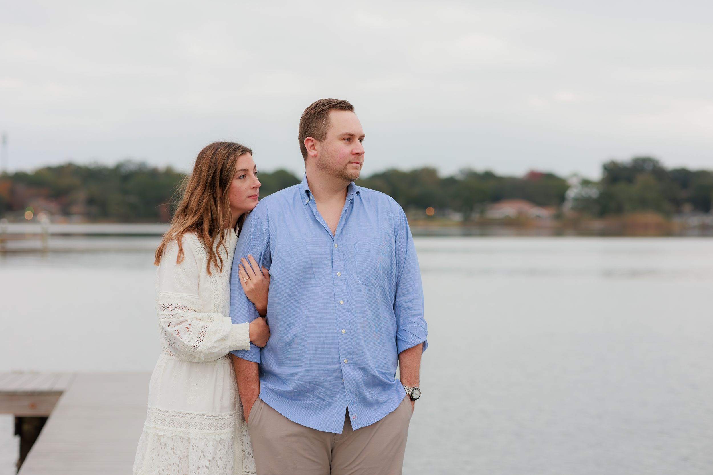 A couple stands together on a dock overlooking a serene lake during an engagement photo session.