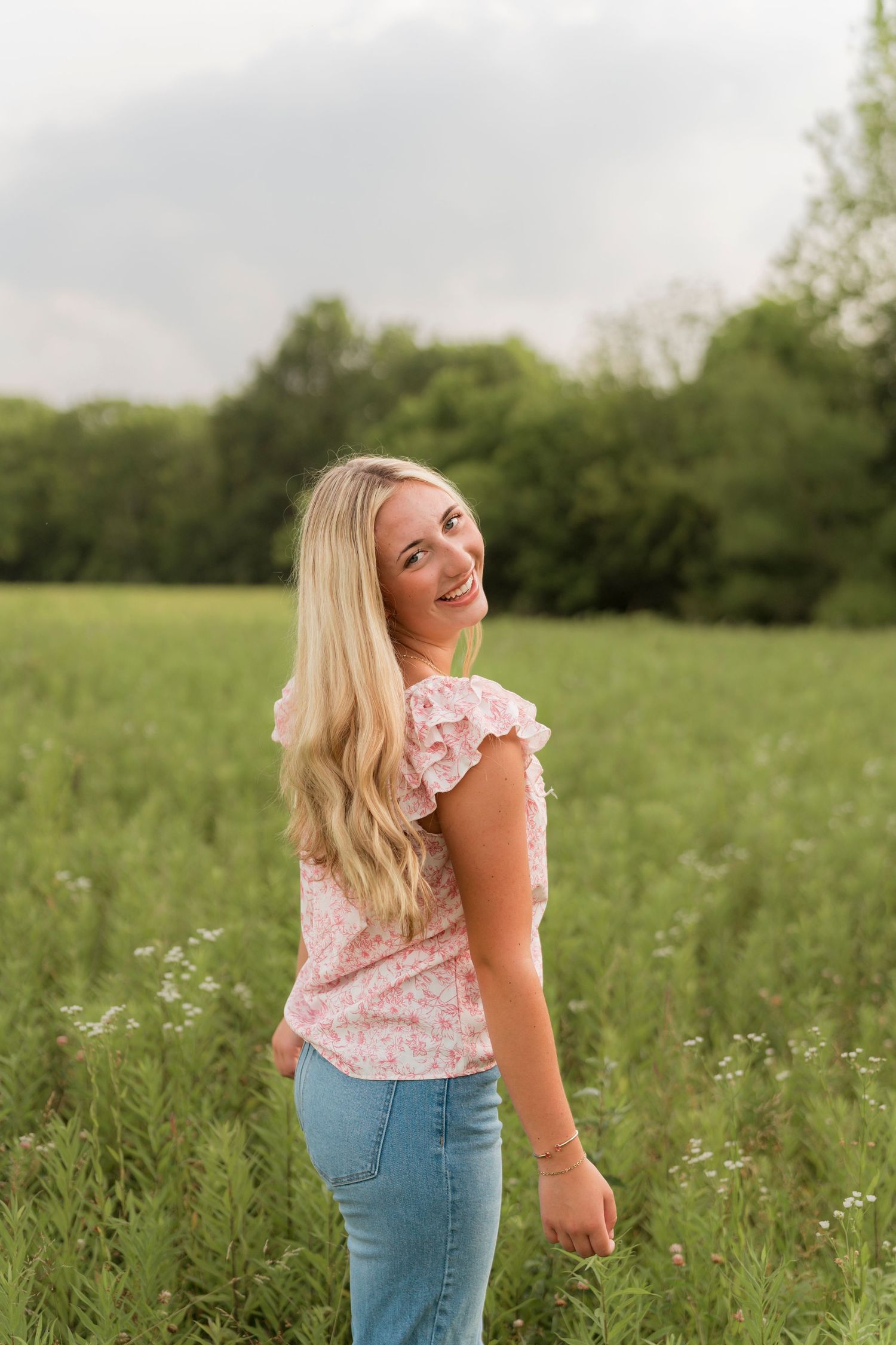 A figure in a white dress walks through a sunny meadow filled with vibrant wildflowers and tall grass.