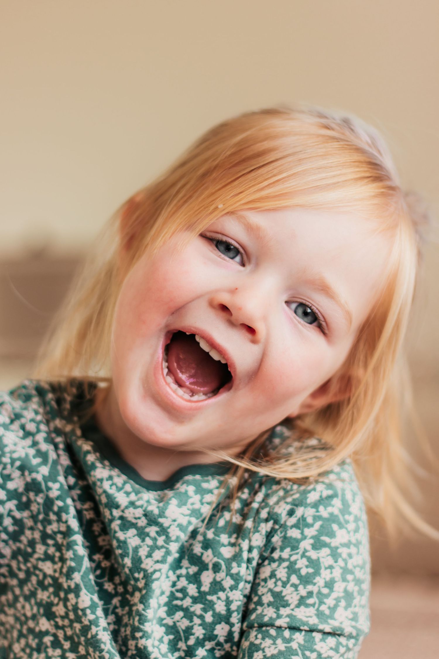 Joyful blonde toddler girl with blue eyes laughing, wearing a green floral dress, portrait photo | Kids Birthday Photo Sessions