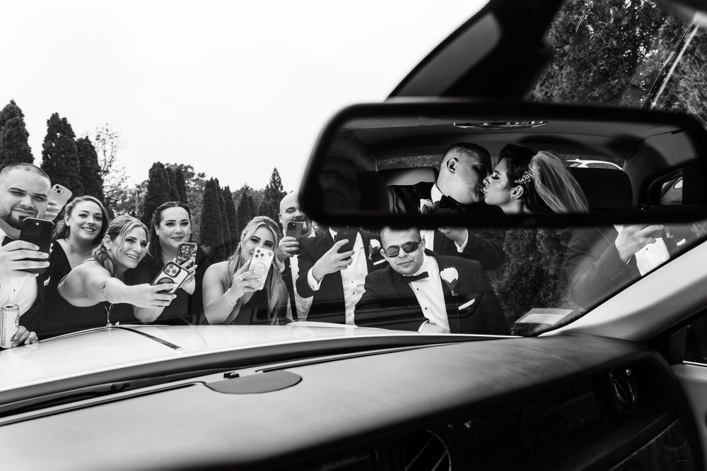 Wedding party peers through car window in playful black and white photograph.
