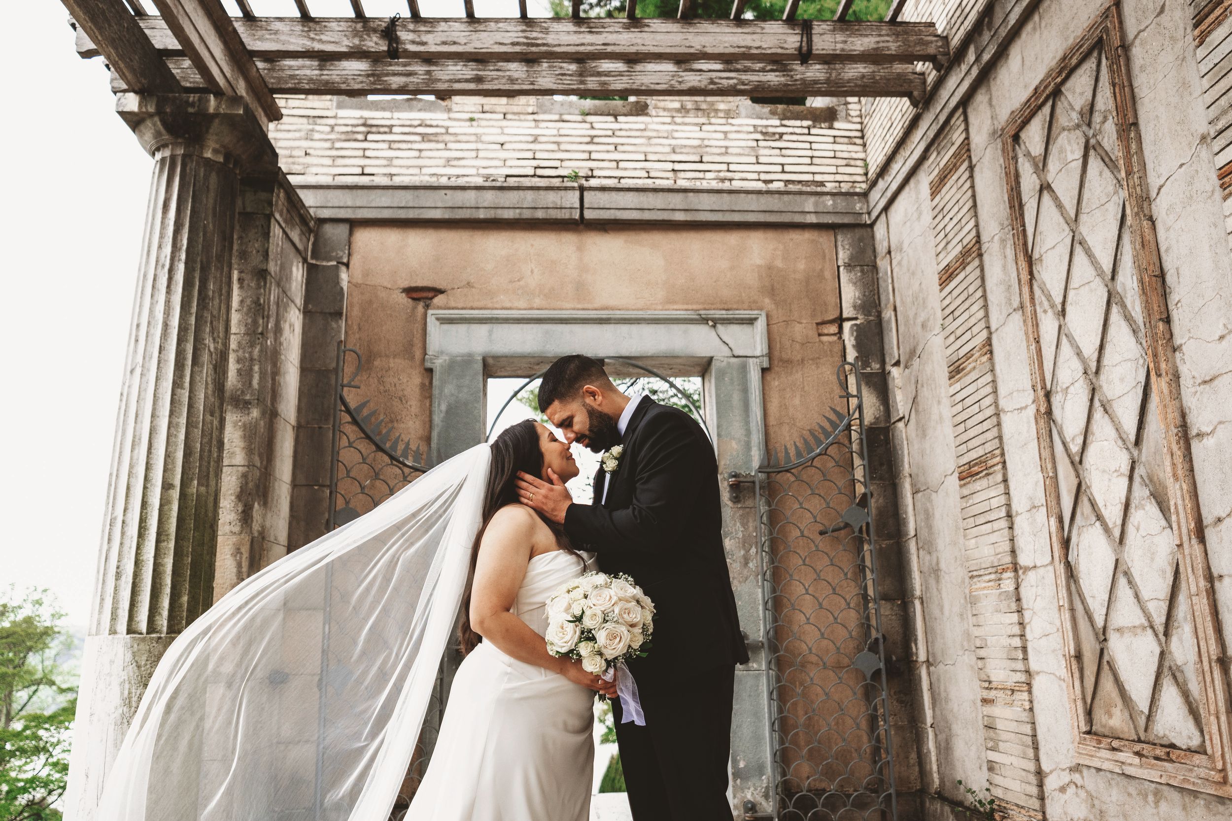 A romantic wedding moment captured under a stone archway with flowing veil.
