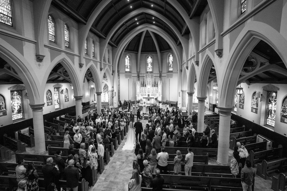 Cathedral wedding ceremony with gothic arches and packed pews in black and white.