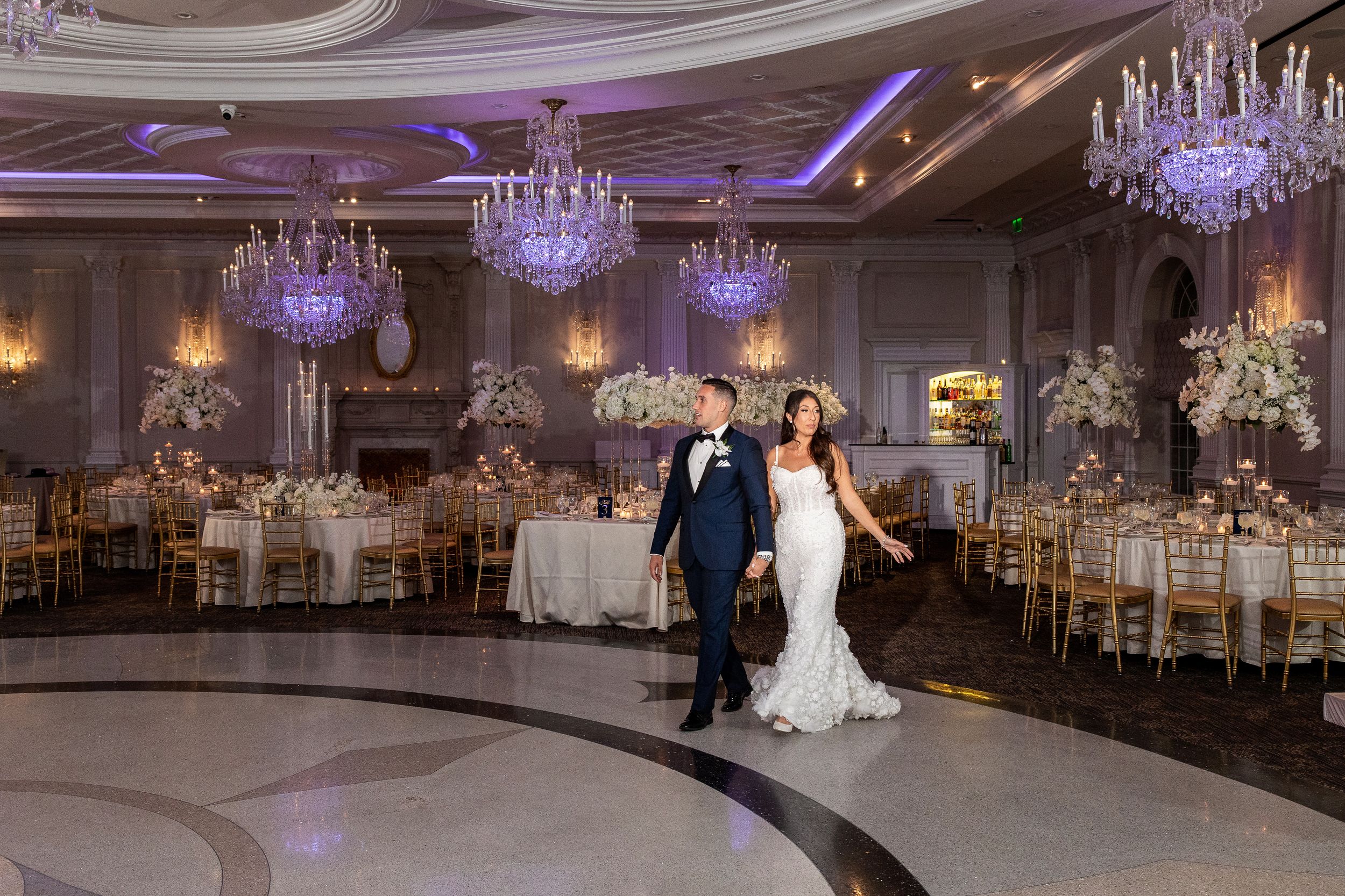 Elegant ballroom wedding reception with crystal chandeliers and ornate decor.