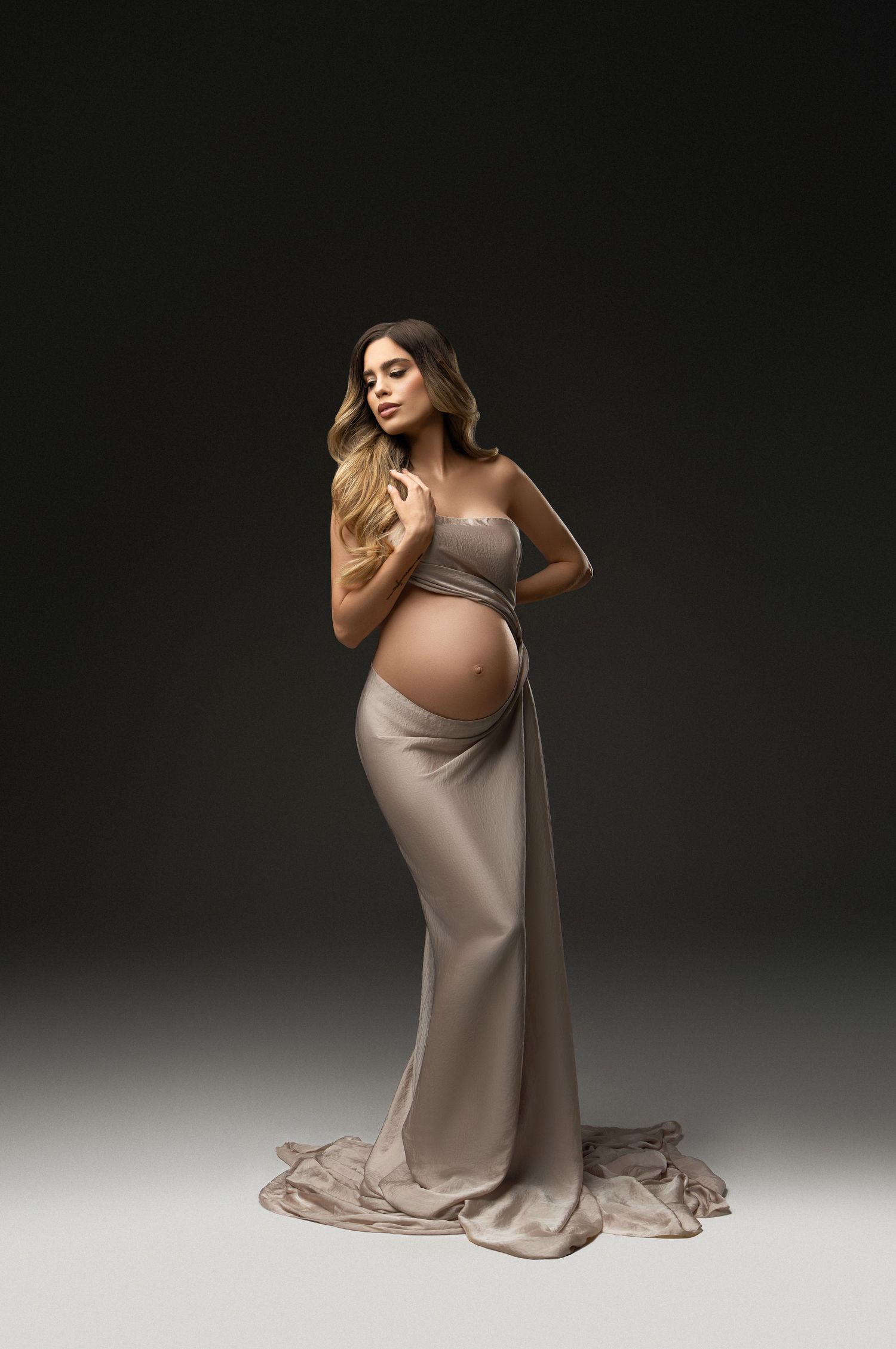 A flowing red maternity gown billows dramatically against a dark background in an elegant pregnancy portrait.