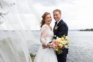 Bilde av brudeparet som ser rett i kamera med vind i sløret og dramtiske skyer.