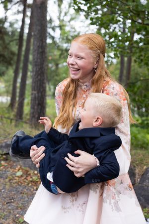 Bilde av en storesøster som løfter lillebror, hun leker og tuller med han. De begge smiler.