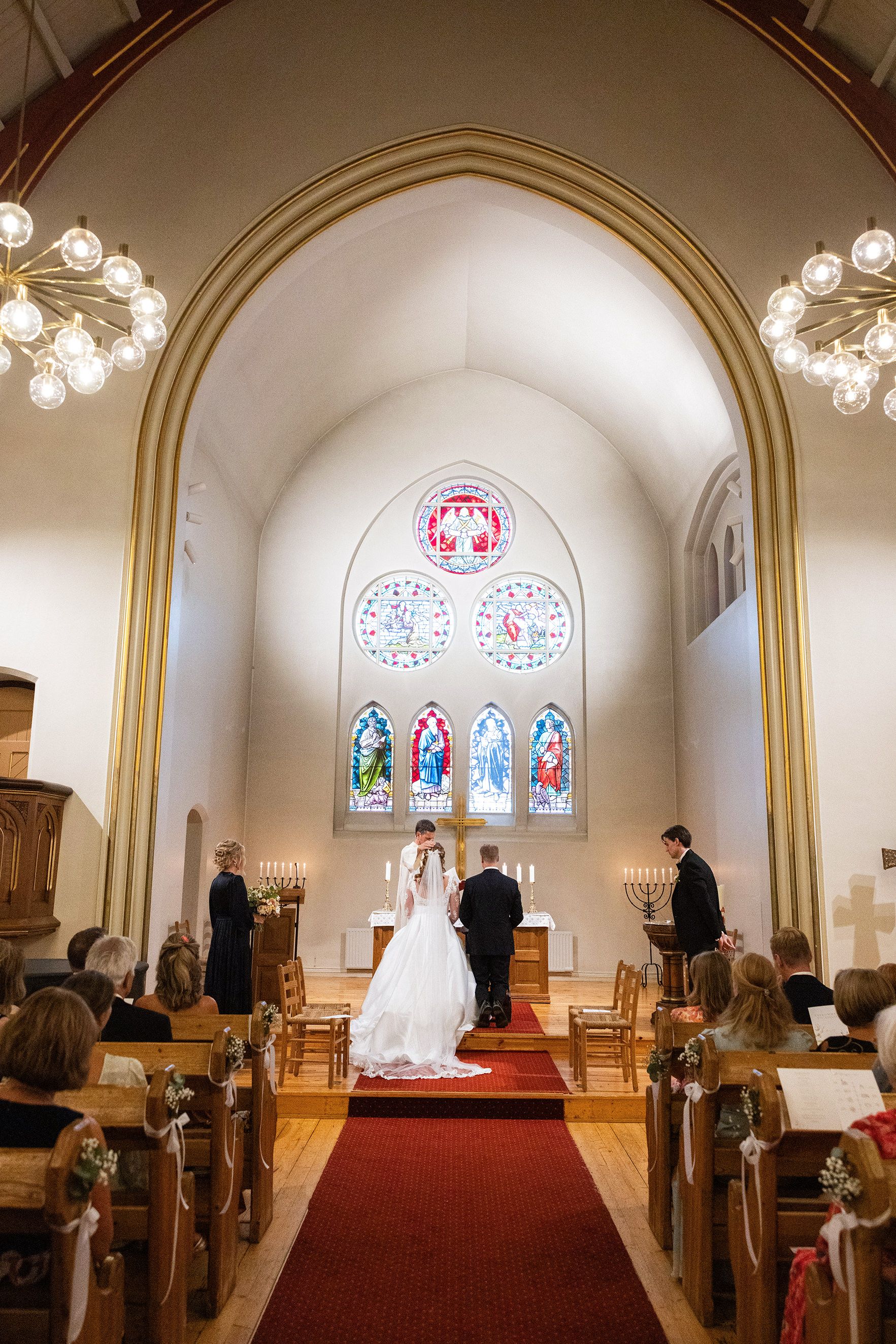 Bildet er tatt inne i en kirke, brudeparet kneler og blir velsignet av presten.