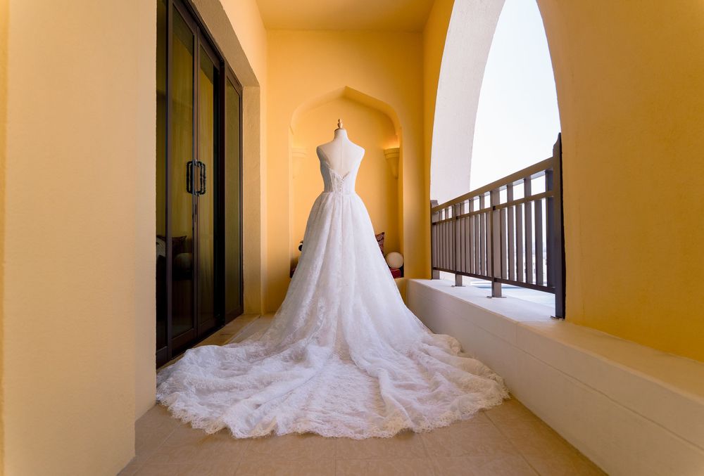 A white wedding dress with a flowing train displayed in an elegant yellow-walled hallway.