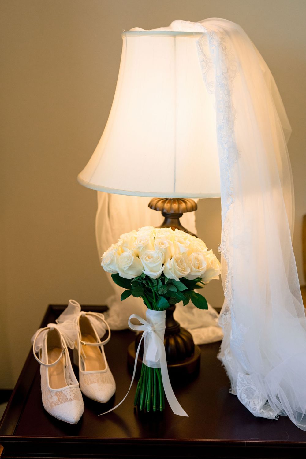 Wedding accessories including white heels, bouquet, veil and table lamp arranged in an elegant display.