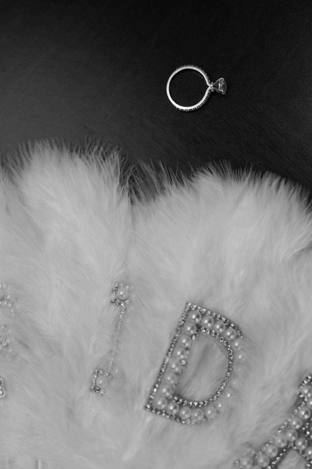 Close-up of white feather trim with sparkly rhinestone letters against a dark background.