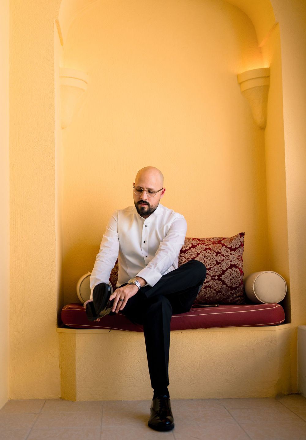 A person in a white shirt and black pants sits on a red cushioned alcove bench against yellow walls.