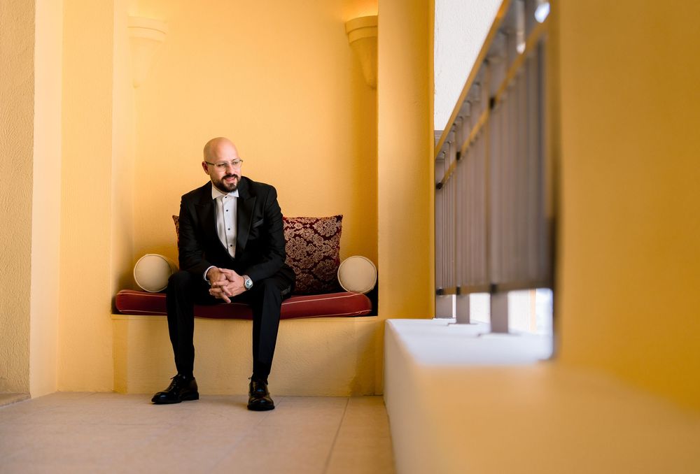 A person sits alone in a minimalist yellow hallway with white columns and natural lighting streaming through windows.