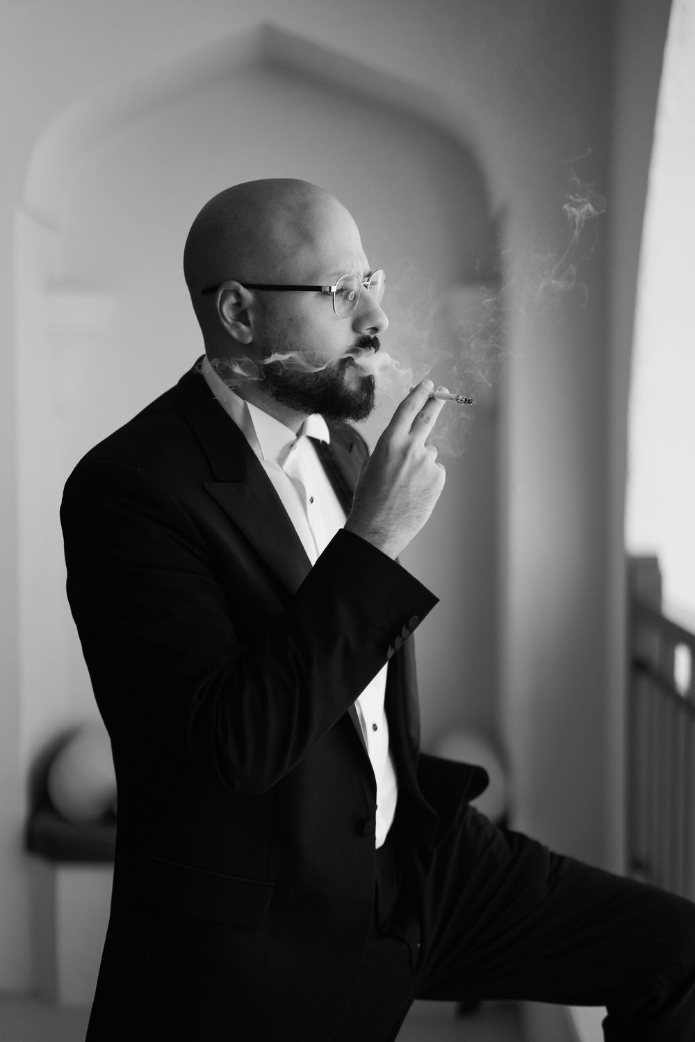 A black and white photo series showing a person in formal attire smoking by a window in dramatic lighting.
