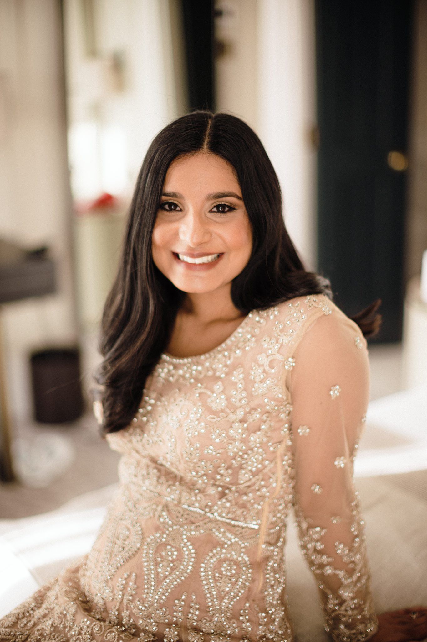 A person wearing a sheer white embroidered dress with delicate floral beadwork and lace details poses elegantly.
