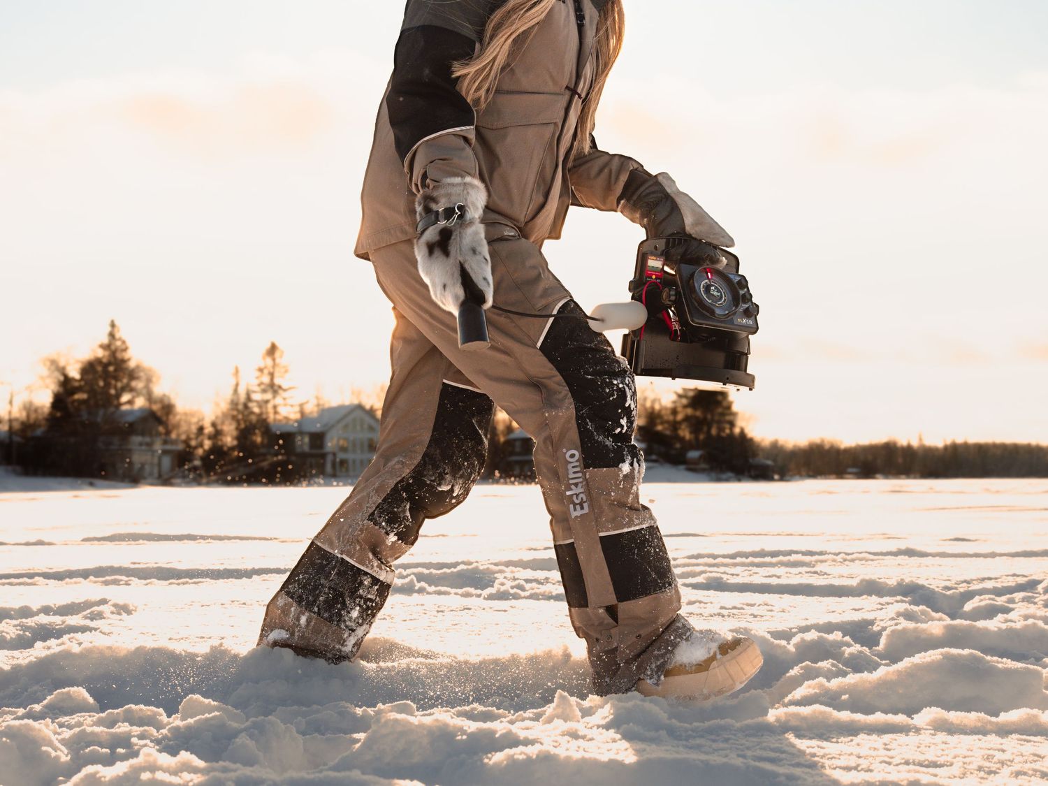 Person walking through deep snow wearing brown winter fishing gear and boots.