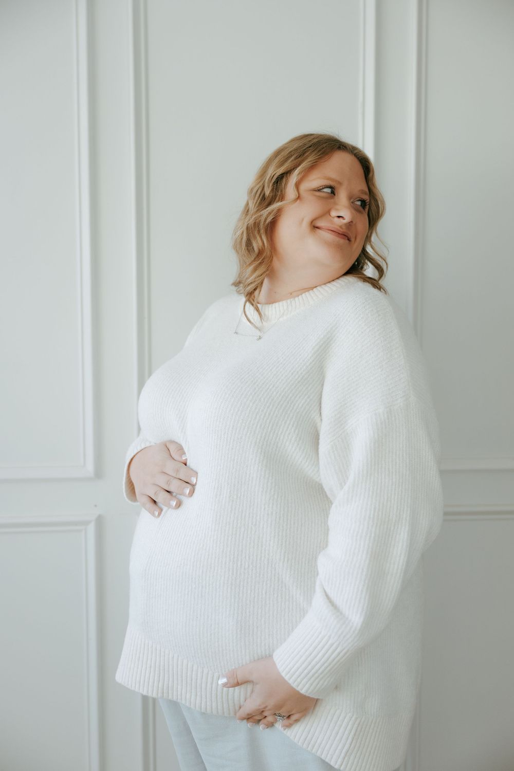 A person wearing a cozy white knit sweater poses against a white wall in a series of minimalist fashion photos.
