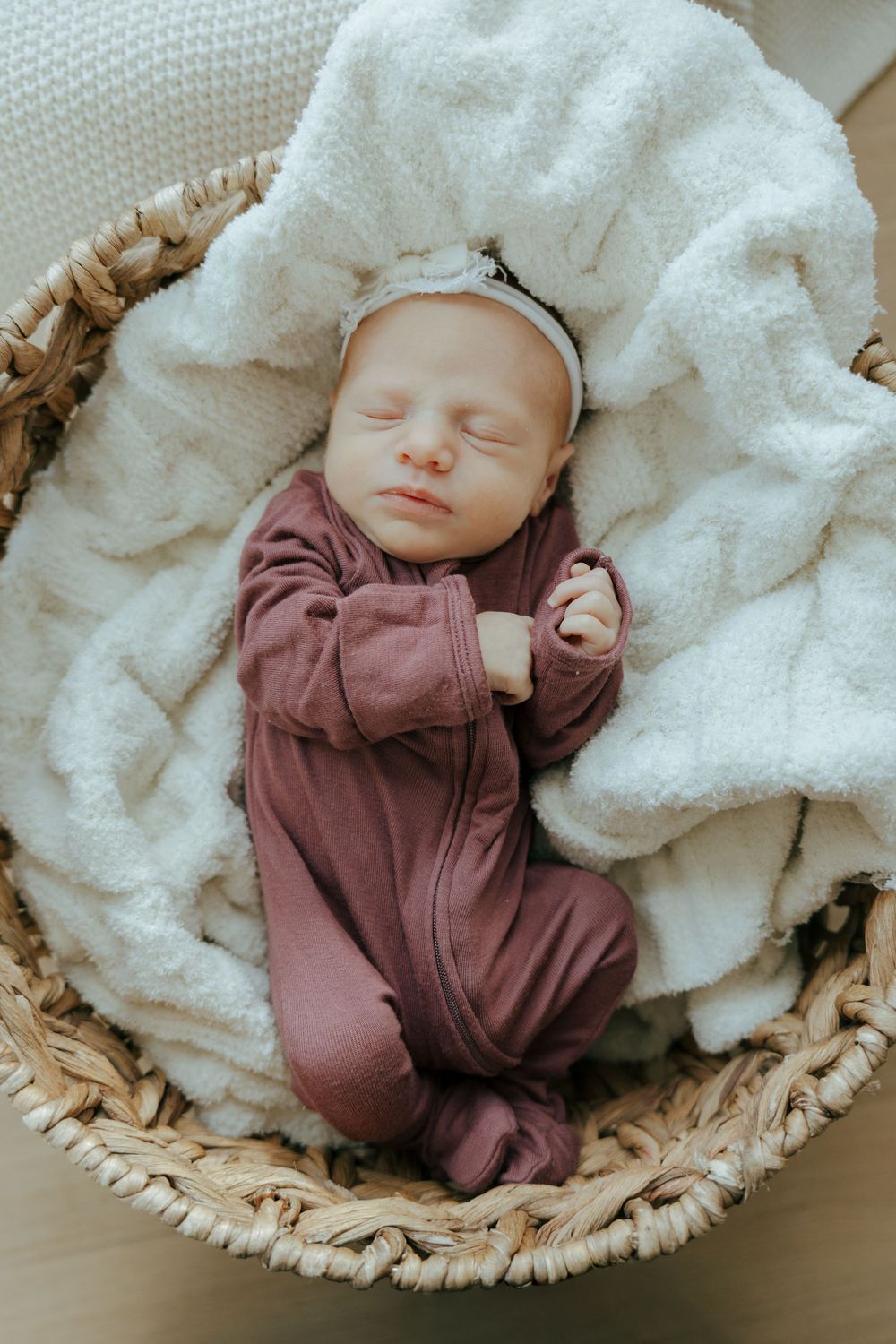A tiny baby rests peacefully in a woven basket lined with soft white blankets.