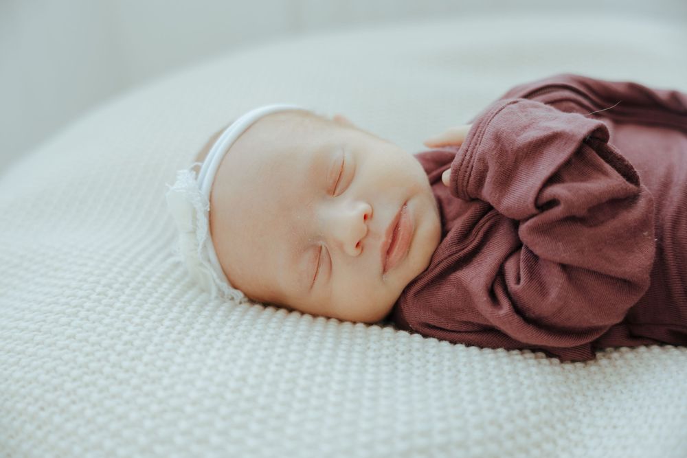 A peaceful sleeping newborn wrapped in brown clothing on a white textured blanket.
