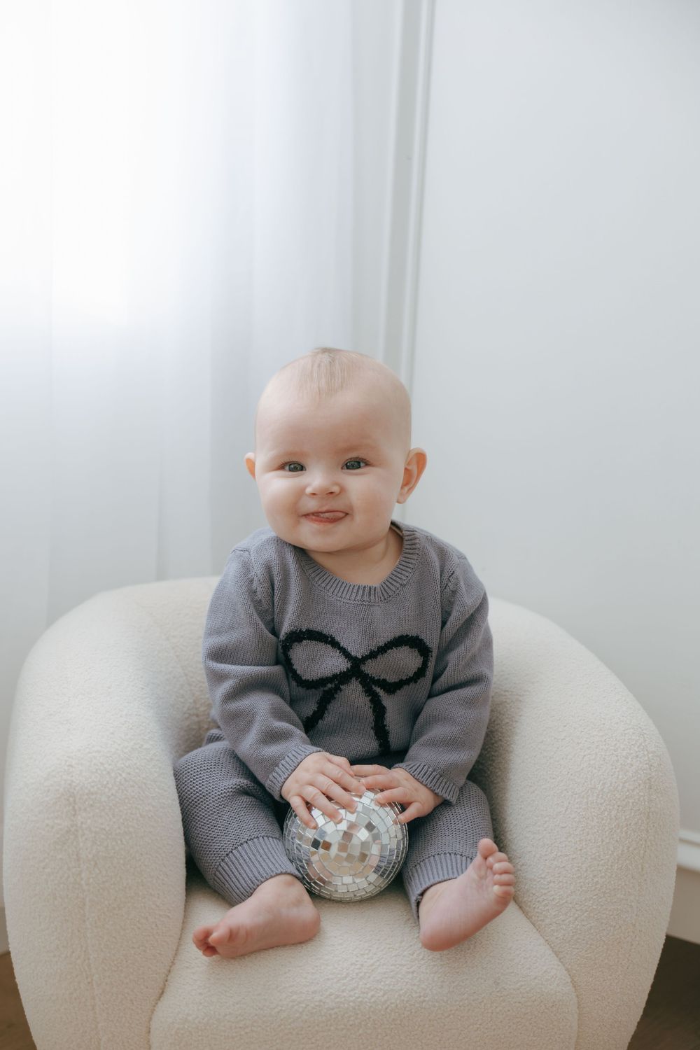 Baby in gray sweater sits on white couch with small bowl in progressive sequence of candid moments.