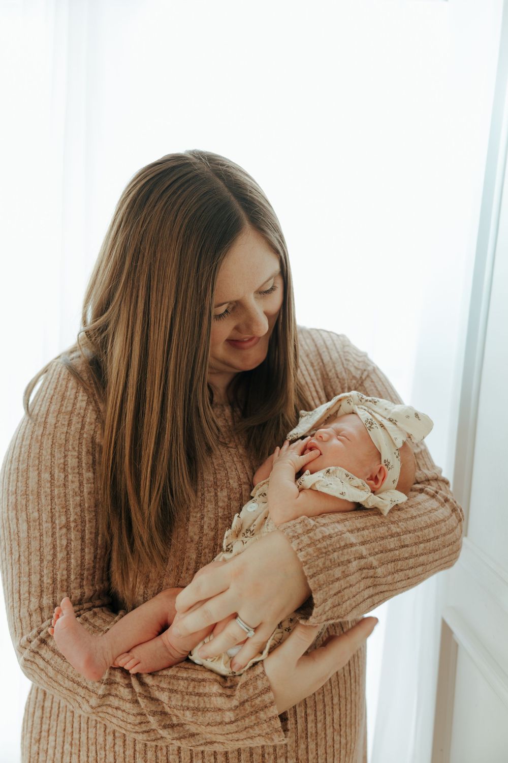 A tender moment of a parent in a knit sweater cradling and bonding with their newborn baby.