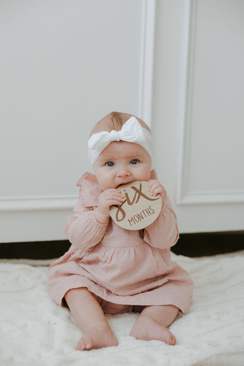 Baby in pink dress sits on white blanket in series of sweet poses.