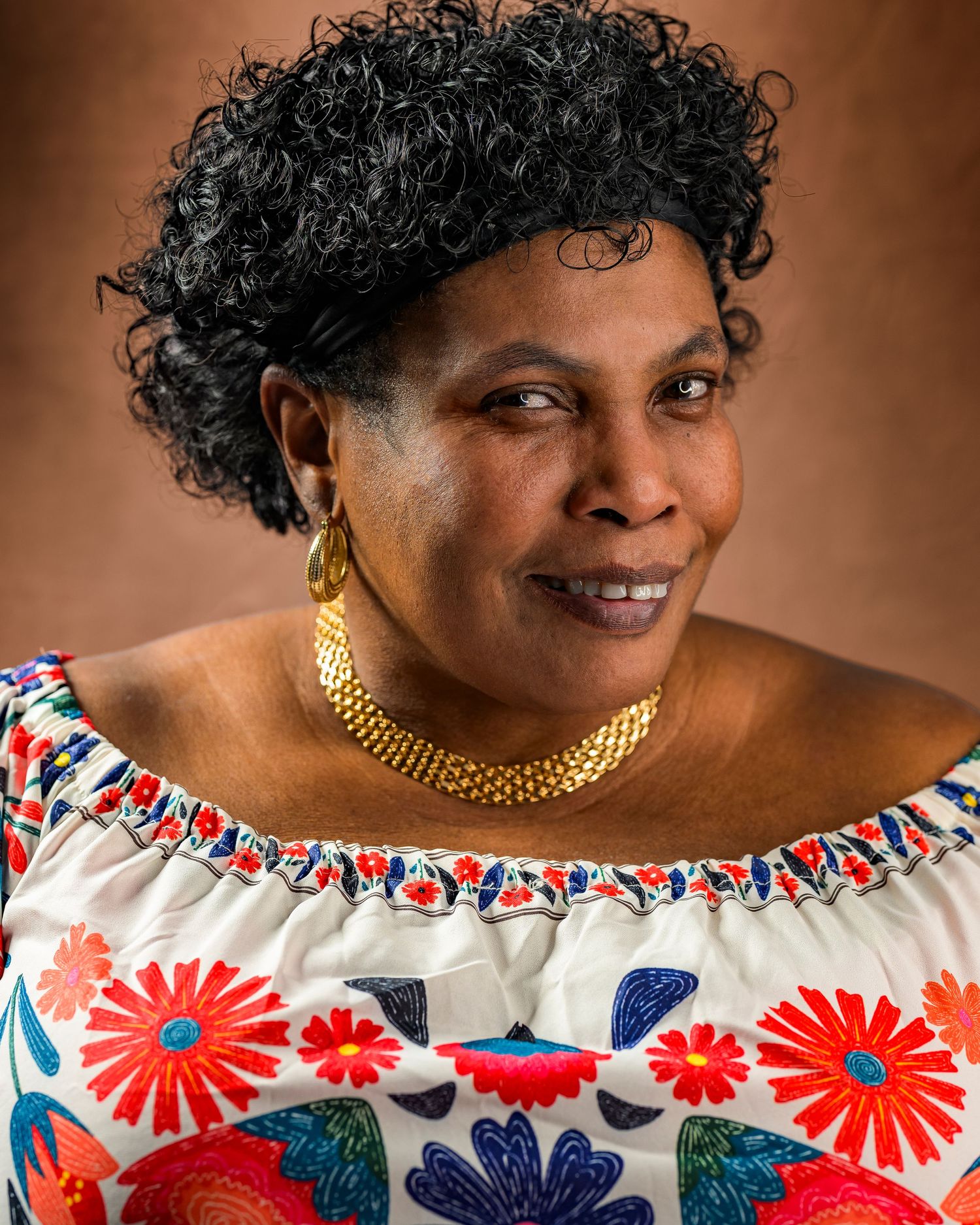 Woman wearing colorful floral off-shoulder top and gold necklace smiling warmly.